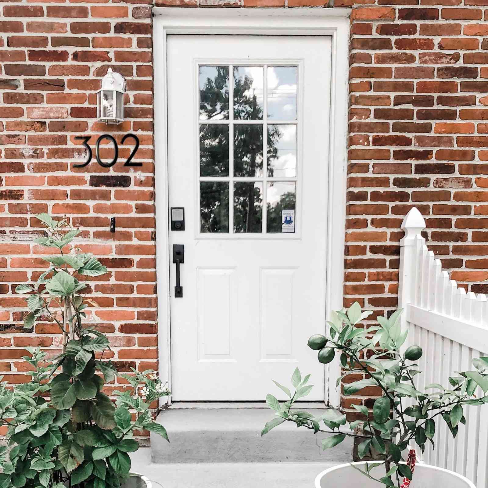Black aluminum number 5 on a brick wall next to a white door for stylish home decor