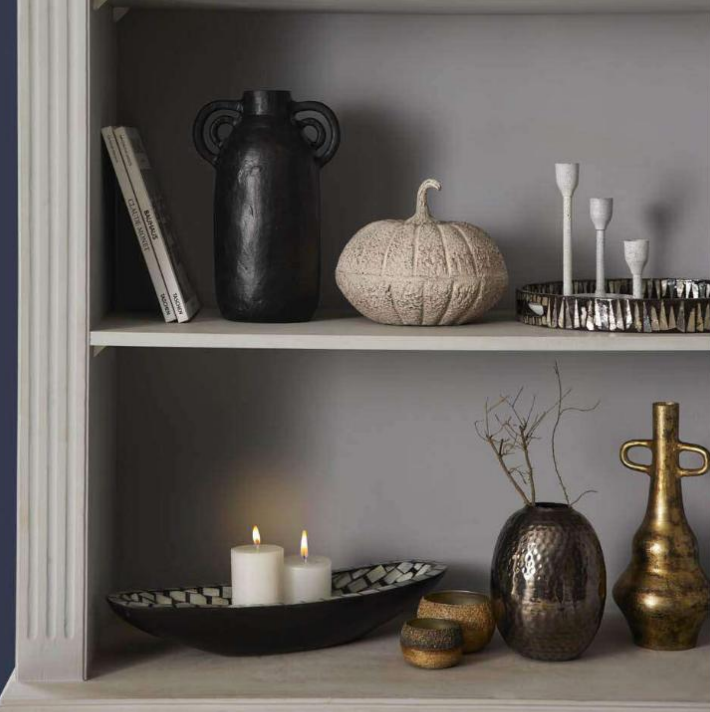 Black aluminum vase on a shelf among decorative items and candles for stylish home decor