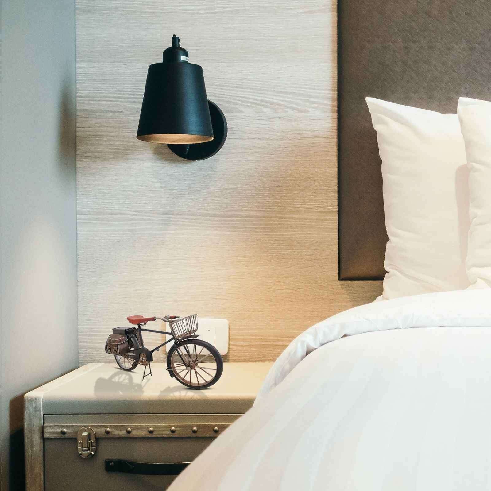 Decorative metal bicycle model placed on a bedside table beside a stylish lamp and bed