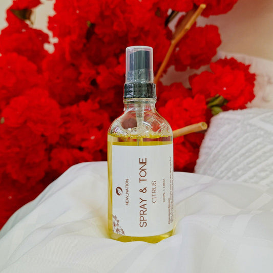 Heav Nation Citrus Body Spray in a clear bottle with a spray nozzle, surrounded by red flowers