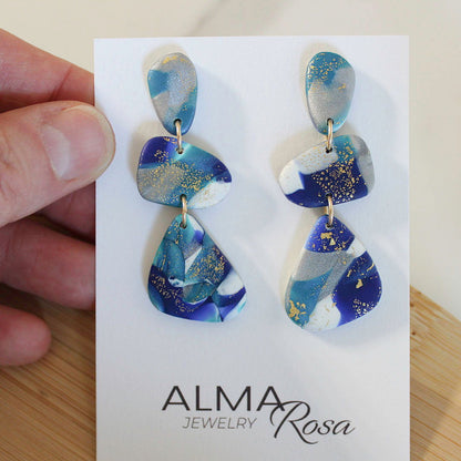 Alma Rosa Jewelry polymer clay stone earrings in blue and gold design, hanging from a display card